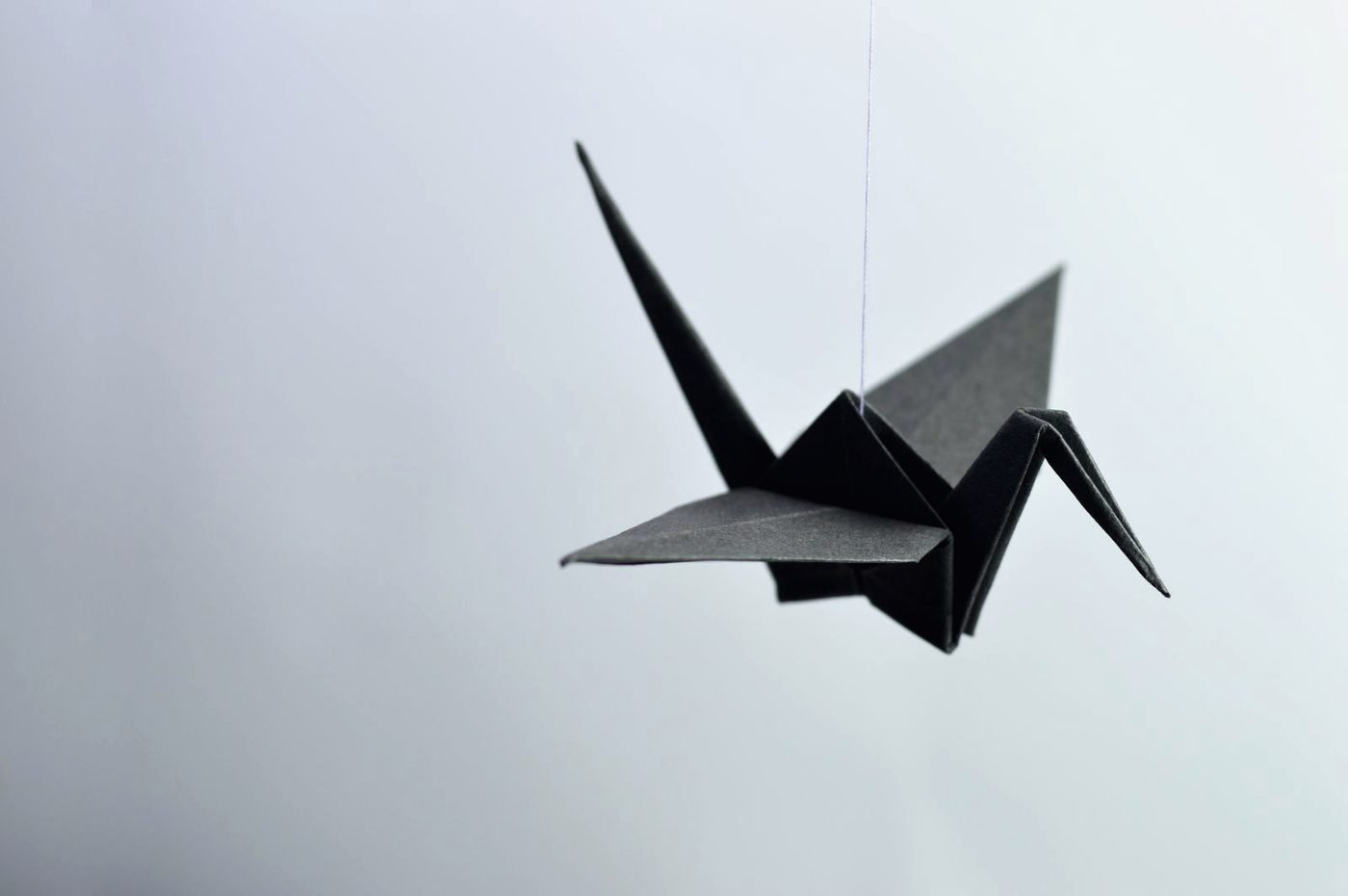 A folded paper crane suspended on a thread against a pale wall.
