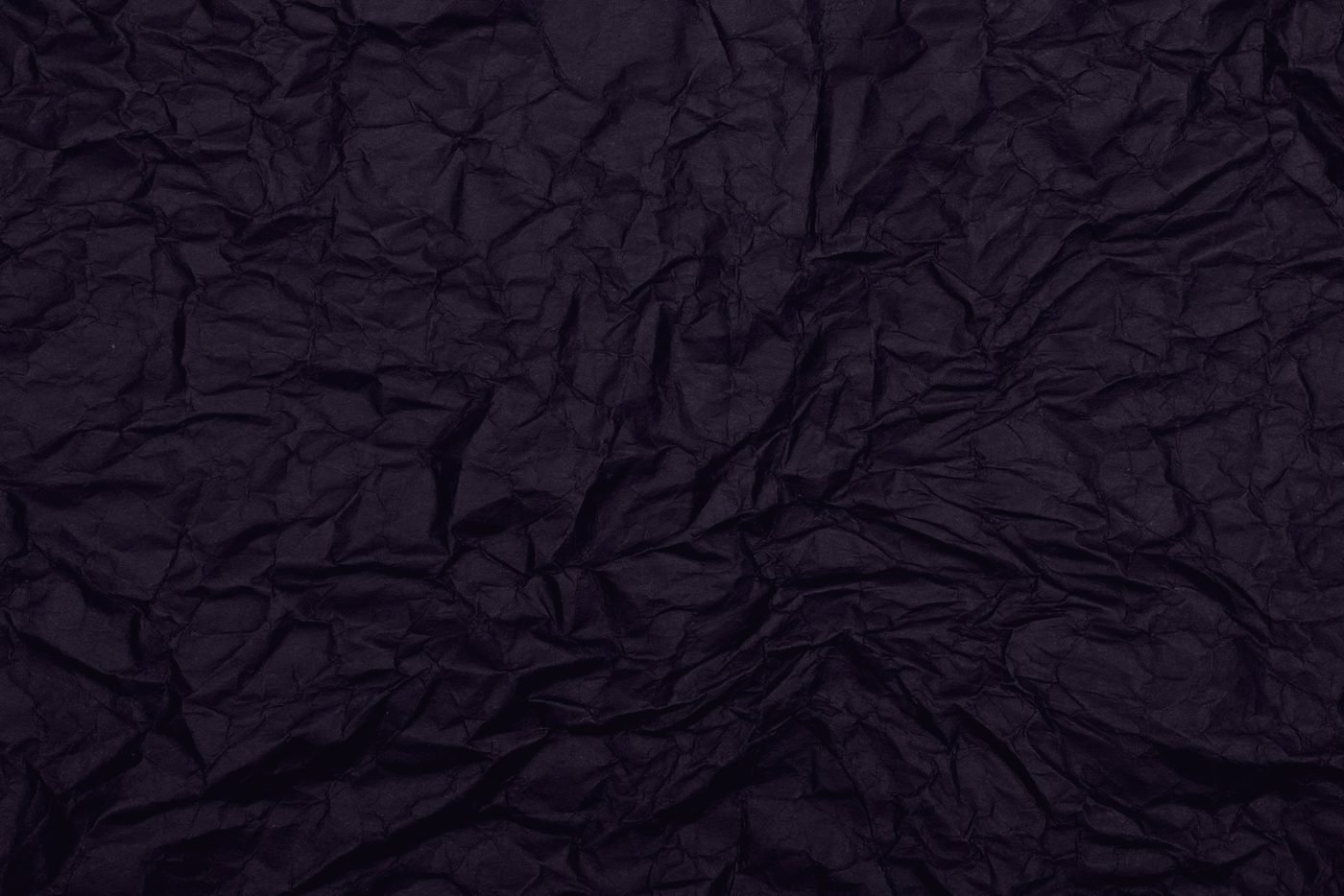 A sheet of paper crushed into a tight ball, deep creases catching a single hard light.