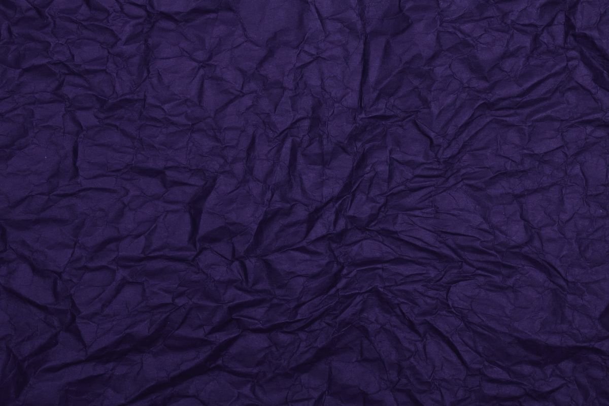 Indigo crumpled paper, the creases holding light along their ridges
