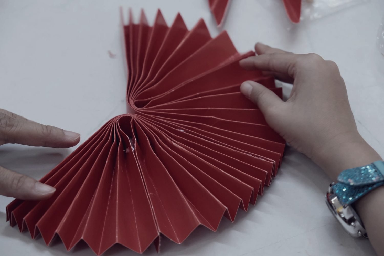 Two hands working a sheet into a fan of identical pleats, every one the same depth as the last.