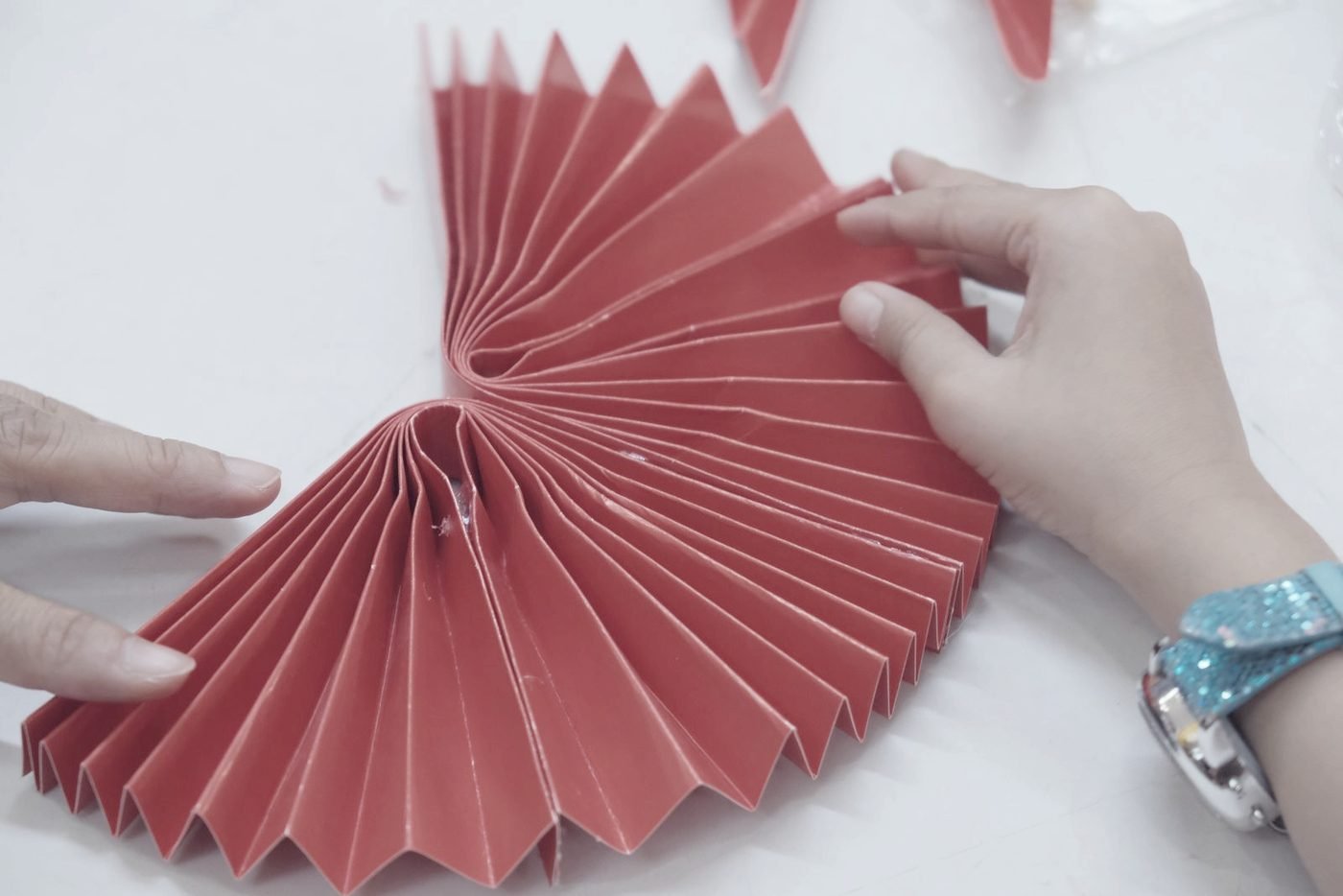 Two hands working a sheet of paper into a fan of identical pleats.
