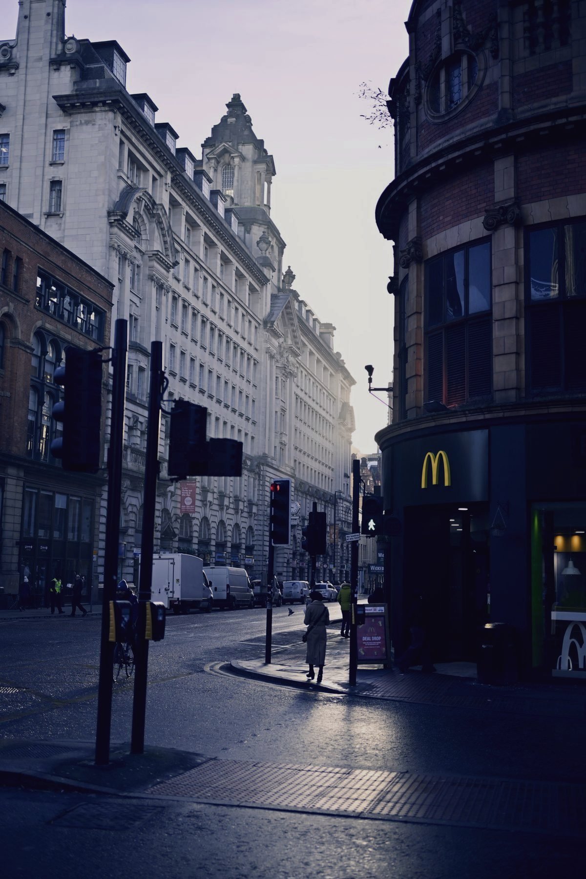 A Manchester street at dusk, red brick buildings and traffic lights reflected on wet road.